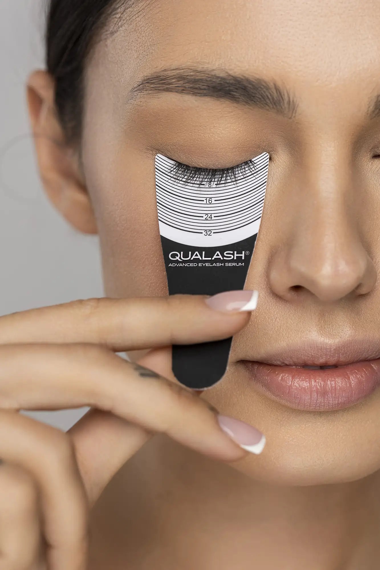 QUALASH® Advanced Eyelash Serum – dark-haired woman measuring lash growth with curved gauge tool