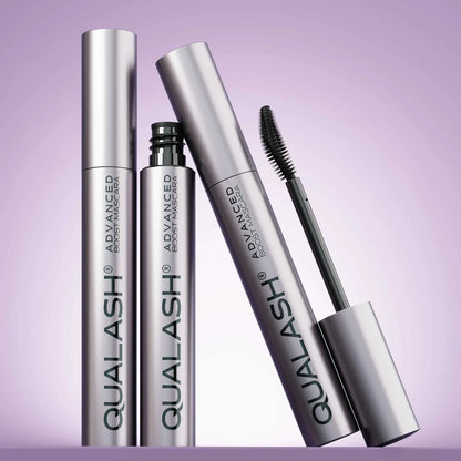 Multiple QUALASH Curl &amp; Lift mascaras arranged creatively on soft purple background with focus on brush and tube